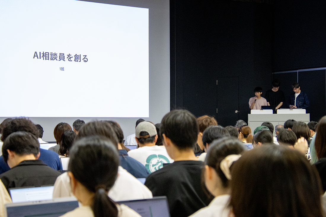 「AI相談員を創る」と表示された画面を前に学生が発表する教室の様子