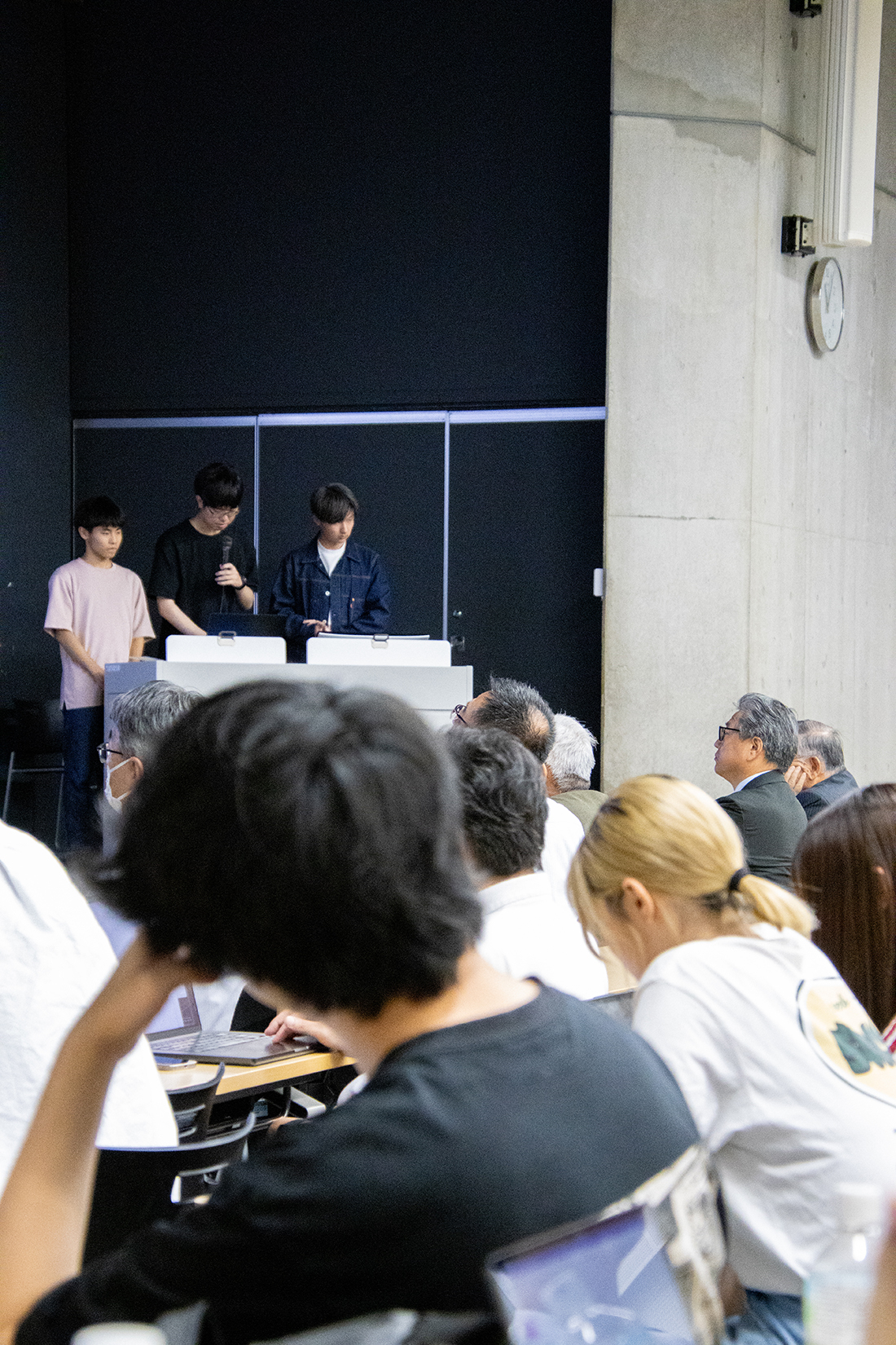 教室内で発表を聞く参加者たち、机にはノートやPCが並ぶ