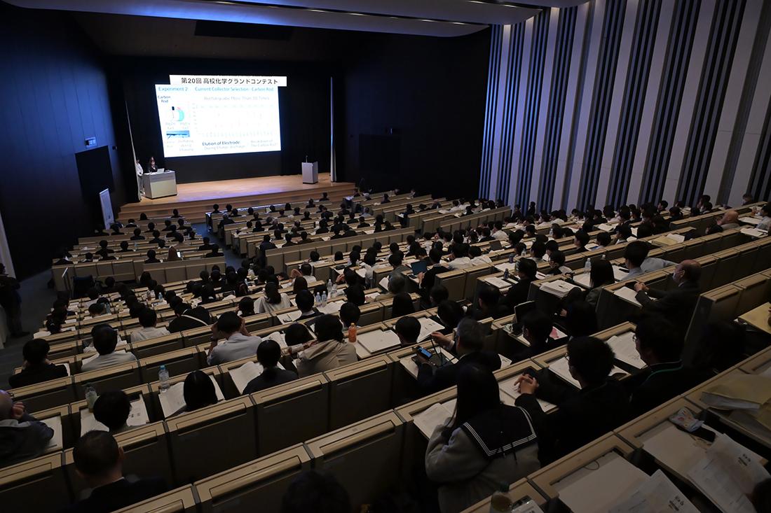 大講堂で研究発表が行われ、多数の聴衆がスクリーンを見ている