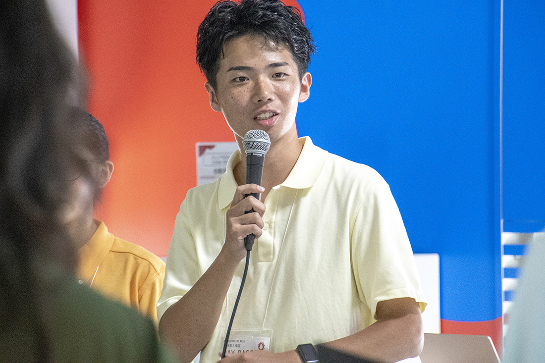 講演中の人物がマイクを持ち、聴衆に向けて話している様子