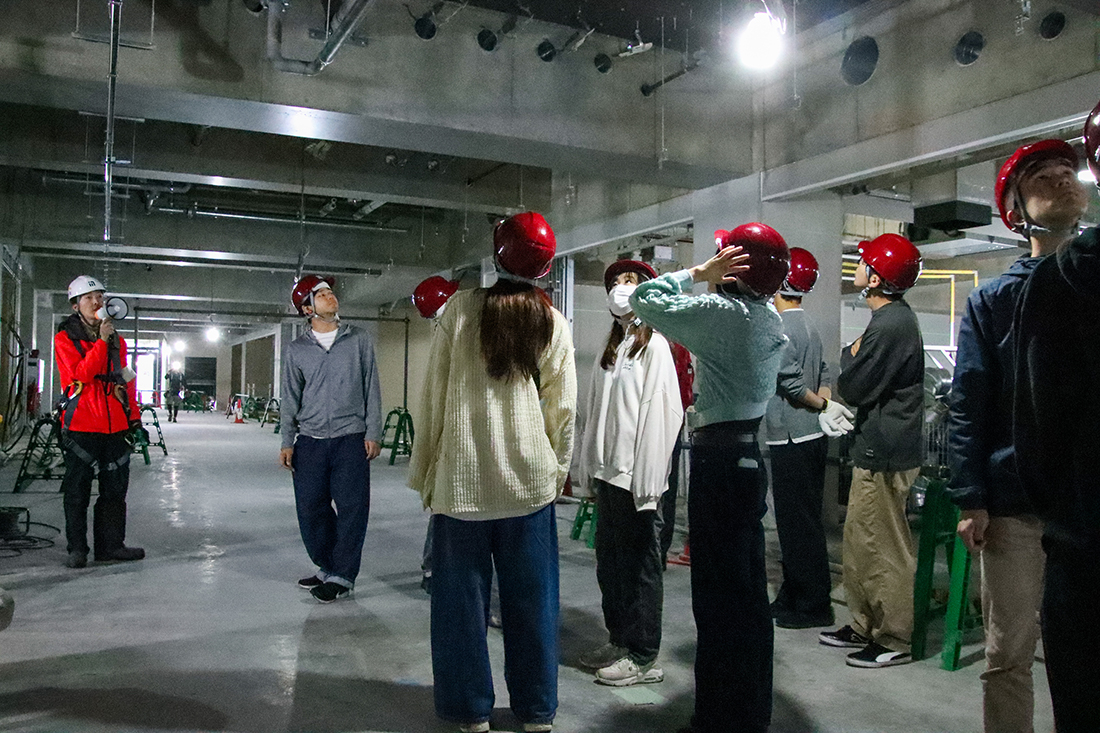 配管や照明がむき出しの現場で見学する人々