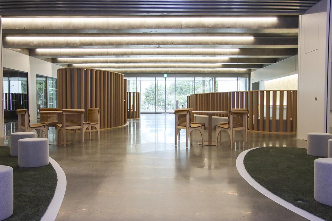 明るいロビー空間。曲線の木製パーティションと椅子・机が配置されている