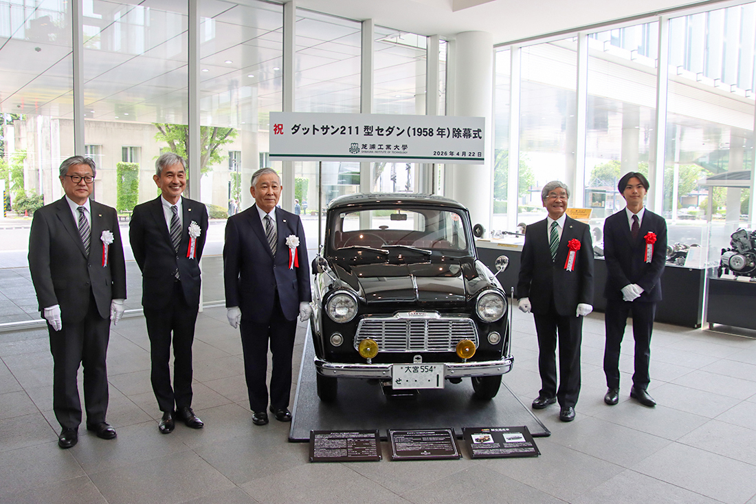 「ダットサン211型」除幕式の看板と、展示車の前で並ぶ参加者