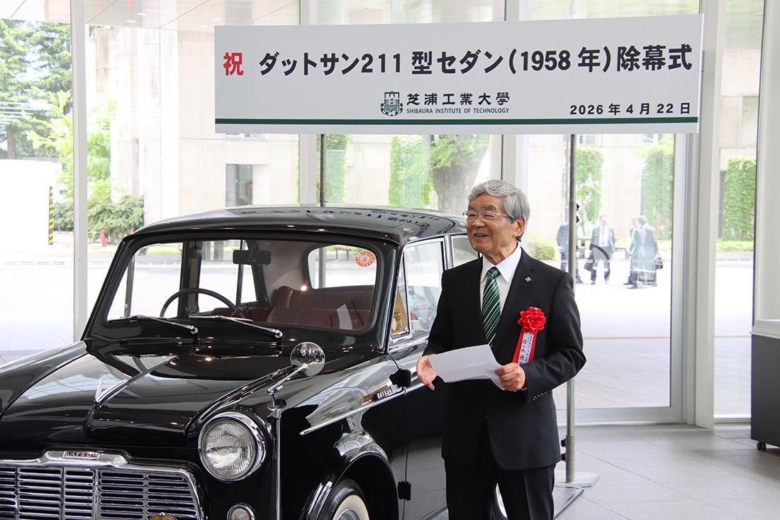 クラシックカーの横で、除幕式の看板を背に佐々木氏があいさつしている