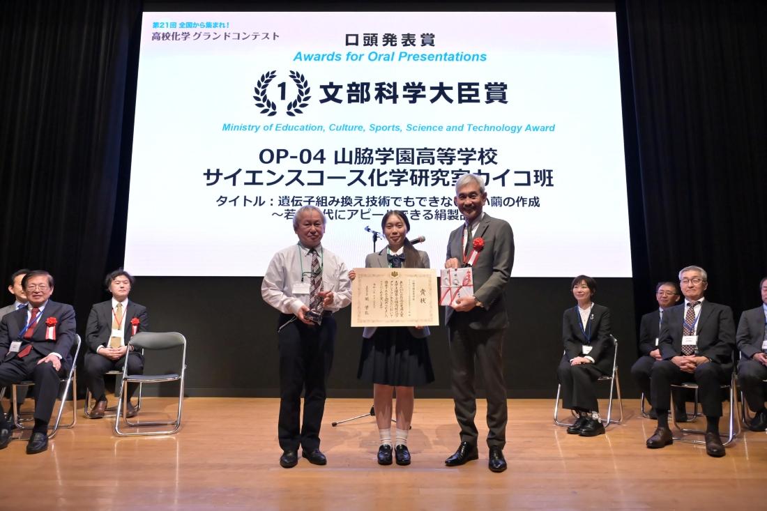 第21回高校化学グランドコンテストの文部科学大臣賞表彰式で、賞状や記念品を持つ3人