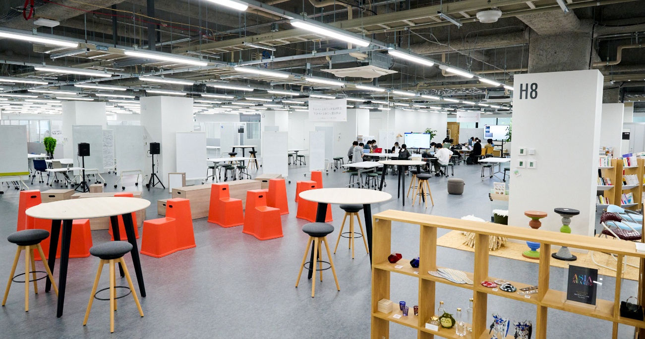 開放的な室内に展示棚とテーブルがあり、利用者が点在している 