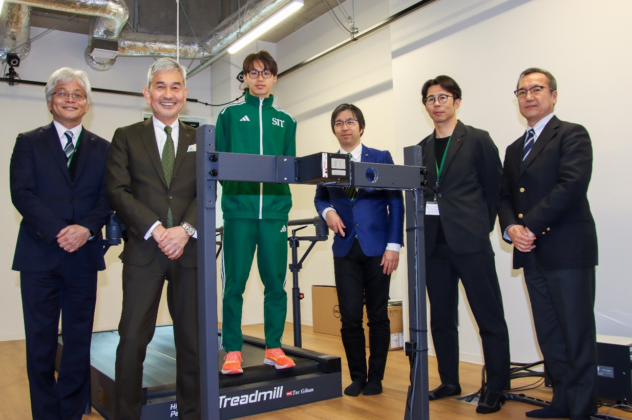 室内に設置されたトレッドミルと計測装置を前に、複数の人が並ぶ様子