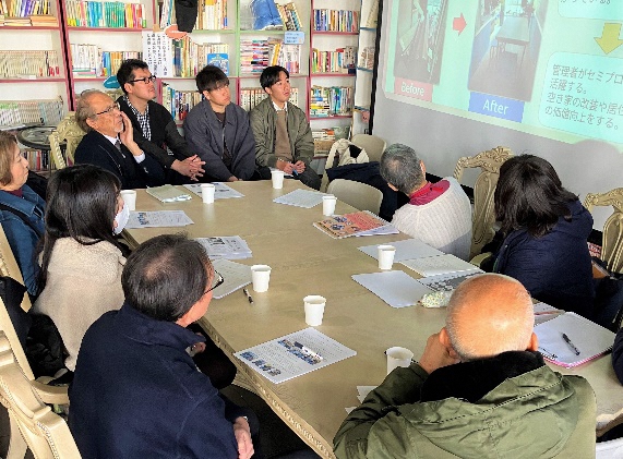 会議風景。参加者がテーブルを囲み、プロジェクターで映像を見ている様子