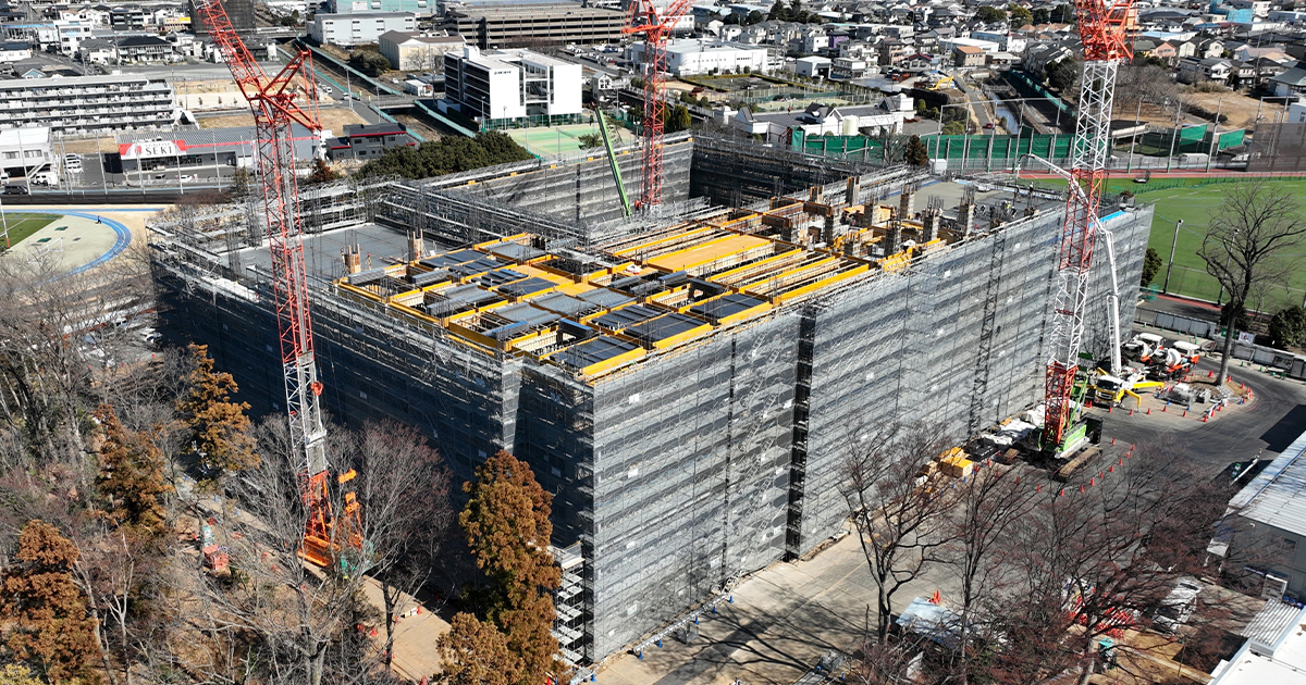 建設中の大型建物を上空から撮影した写真。周囲にはクレーンが設置され、建物は足場とシートで覆われている